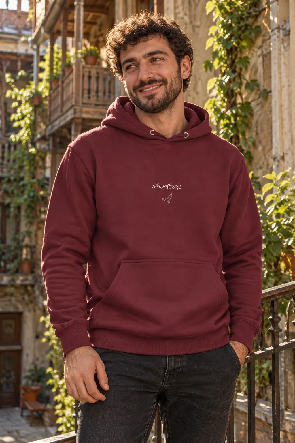 Man smiling in the Araushavs hoodie on a Tbilisi balcony